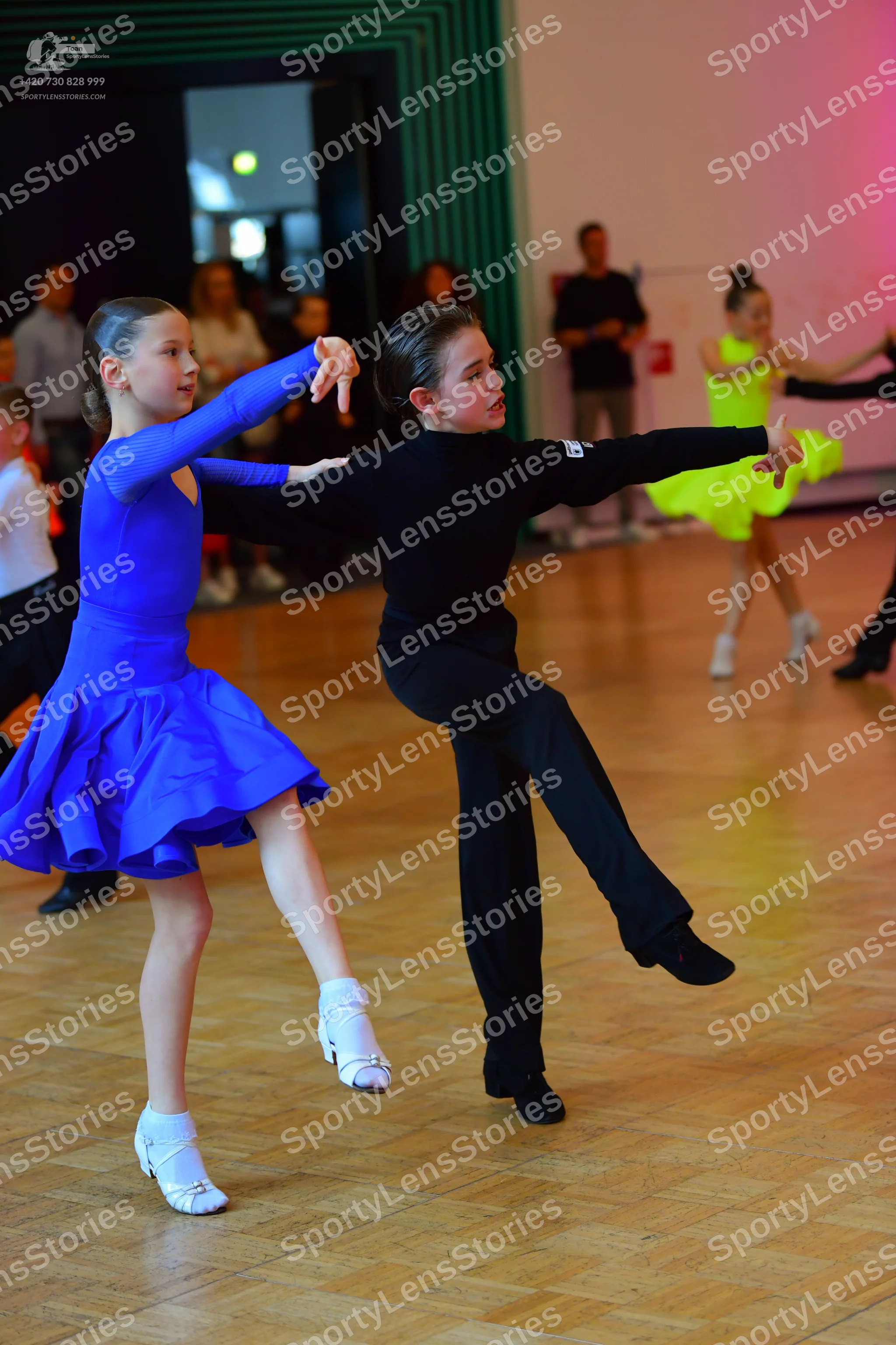 Dancesport competitor: Female dancer in foreground: blue long-sleeved latin dress with a short flared s