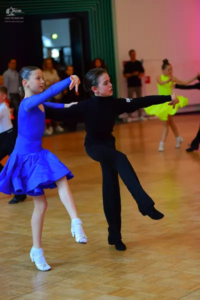 Dancesport competitor: Female dancer in foreground: blue long-sleeved latin dress with a short flared s
