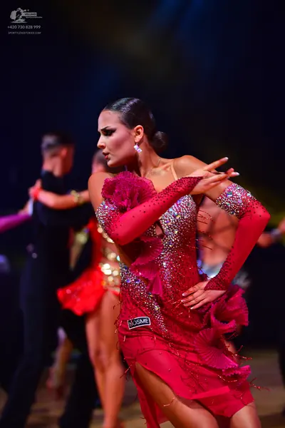Dancesport competitor: Female dancer in foreground: red latin dress with sequins, ruffles, and long sle