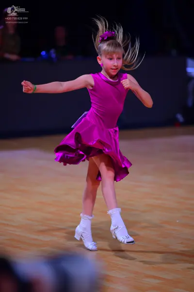 Dancesport competitor: Female dancer: magenta satin-like latin dress with a flared, ruffled skirt and h