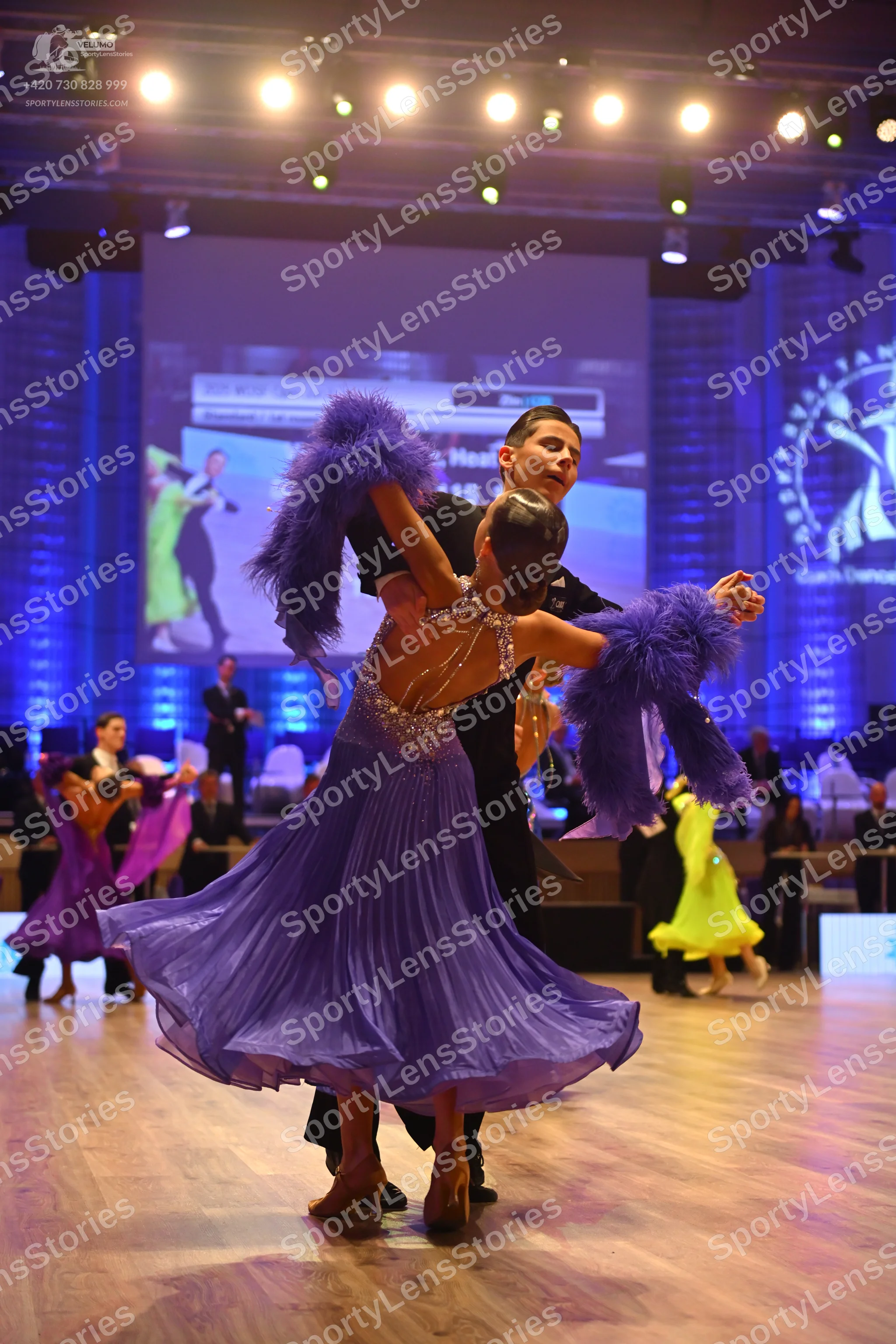 Dancesport competitor: Foreground female dancer: purple latin dress with a sequined/beaded bodice and l
