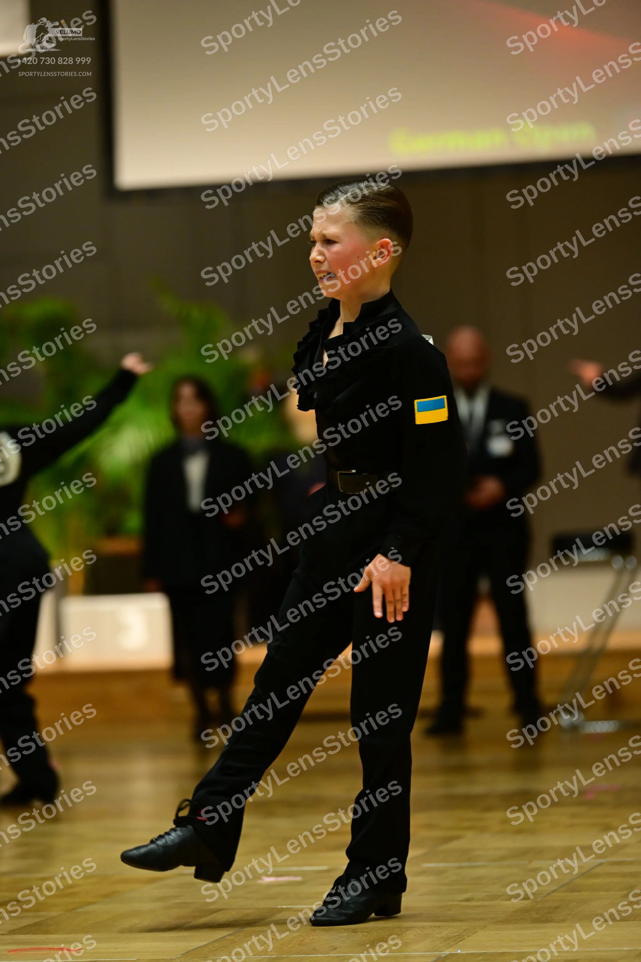 Dancesport competitor: Male dancer: black long-sleeved top with a ruffled collar and a Ukrainian flag p