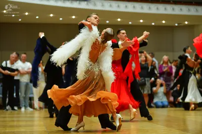 Dancesport competitor: Foreground female dancer: champagne-colored ballroom gown with voluminous white 