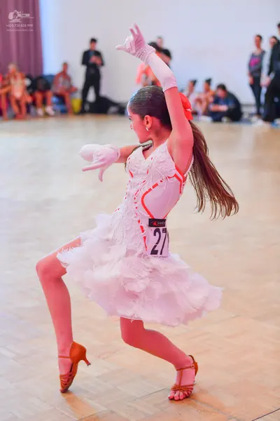 Dancesport competitor #27: Female dancer: white latin dance costume with orange/red trim, a voluminous whit