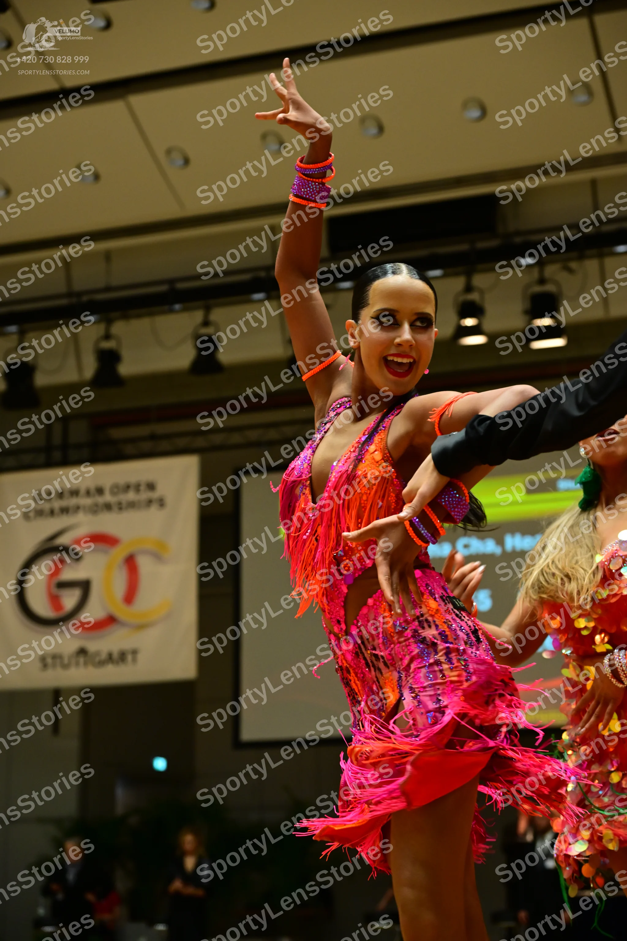Dancesport competitor: Female dancer: bright pink and orange Latin dress with long fringe and sequins,