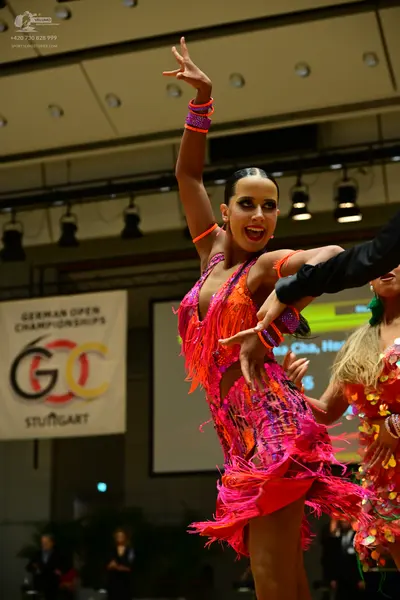Dancesport competitor: Female dancer: bright pink and orange Latin dress with long fringe and sequins, 