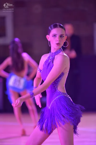 Dancesport competitor: Female dancer (foreground): purple latin dress with rhinestones and fringe skirt
