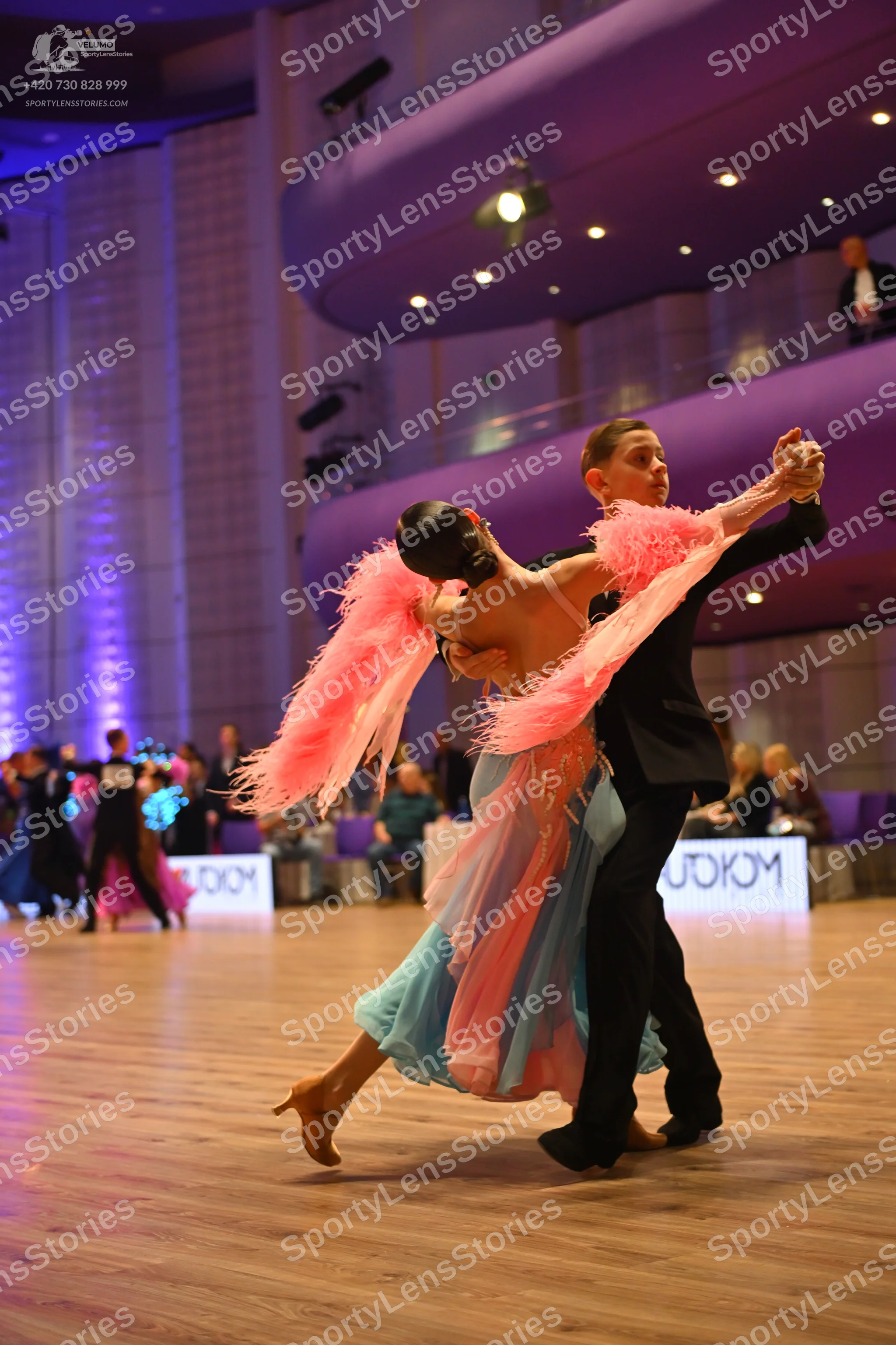 Dancesport competitor: Female dancer: light blue flowy dress with large pink feather-like accents
