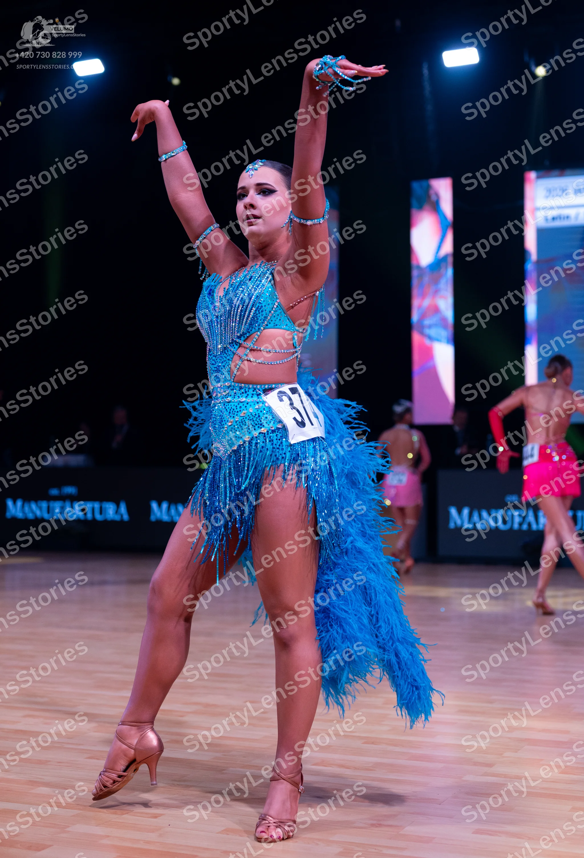 Dancesport competitor: Female dancer in foreground: bright blue latin dance dress with sequins, beads,