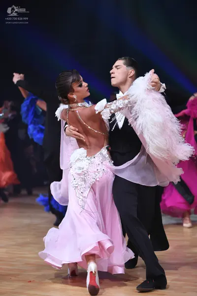 Dancesport competitor: Female dancer: light pink ballroom dress with a flowing skirt, sheer elements, a