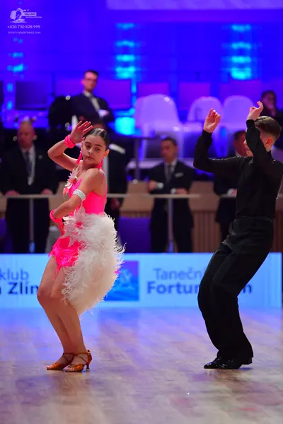 Dancesport competitor: Female dancer: pink Latin dress with white feather-like trim and pink wristbands