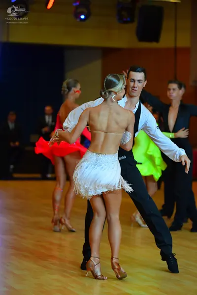 Dancesport competitor: Female dancer in foreground: white latin dress with sequins and fringe and a nud