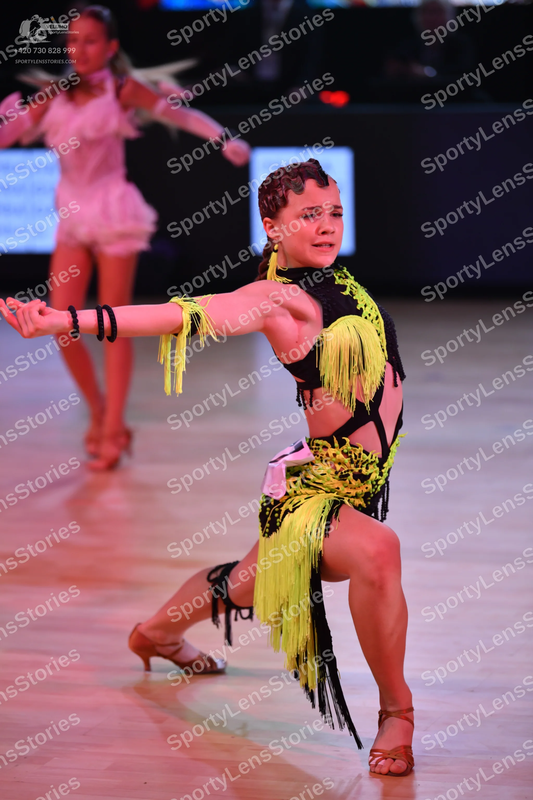 Dancesport competitor: Foreground dancer: black and lime green latin dress with long fringe and cutouts