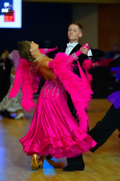 Dancesport competitor: Female dancer: bright pink/magenta dress with large pink feather trim, a sequine