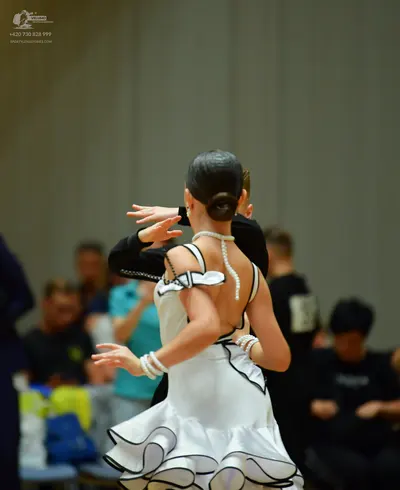 Dancesport competitor: Female dancer: white latin dress with black trim, a ruffled skirt, pearl-like em