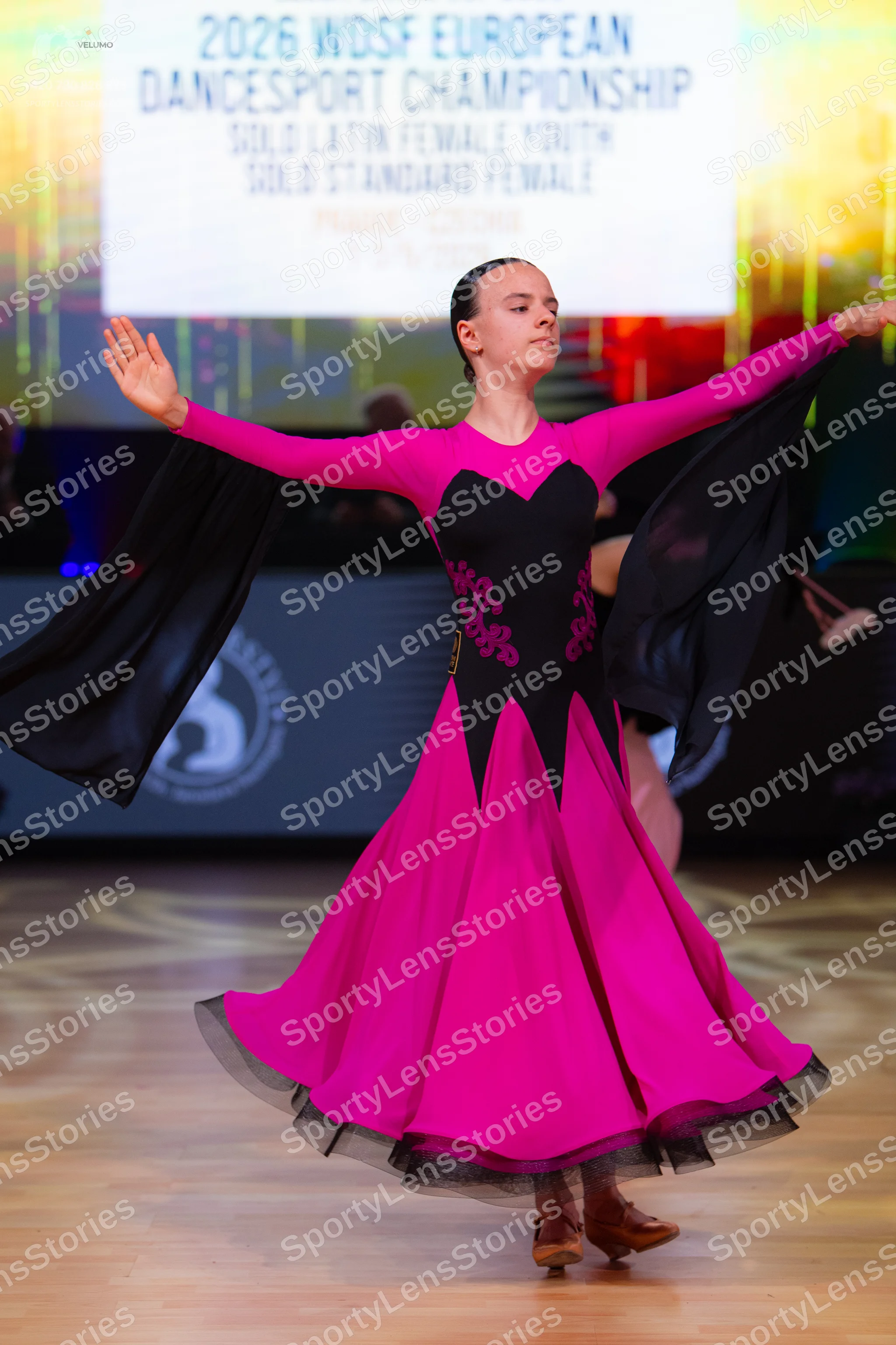 Dancesport competitor: Female dancer: pink and black long-sleeved ballroom dress with a large flowing s