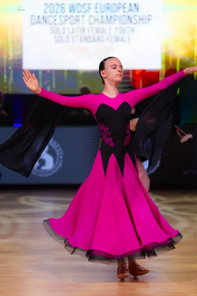 Dancesport competitor: Female dancer: pink and black long-sleeved ballroom dress with a large flowing s