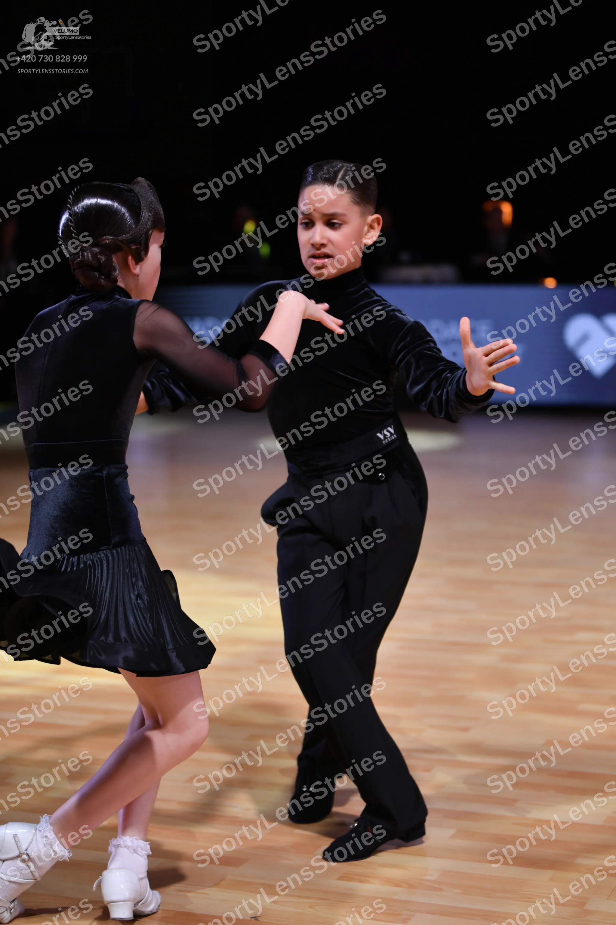 Dancesport competitor: Female dancer: black latin dress with sheer long sleeves and a pleated skirt, wo
