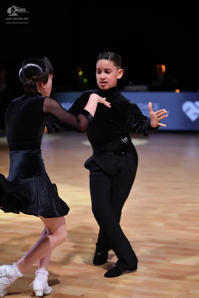Dancesport competitor: Female dancer: black latin dress with sheer long sleeves and a pleated skirt, wo