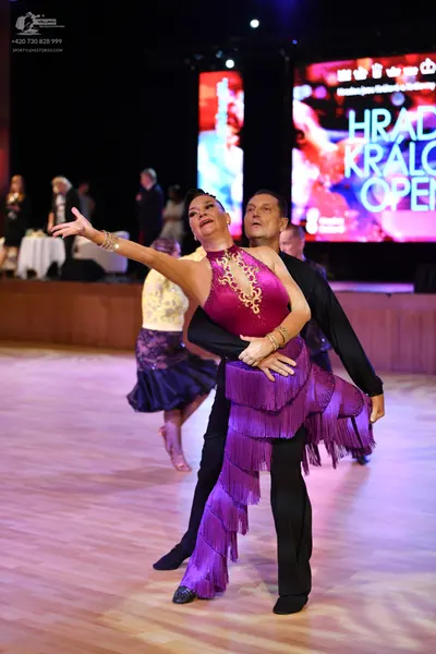 Dancesport competitor: Female dancer in foreground: magenta Latin dress with gold embellishments and lo