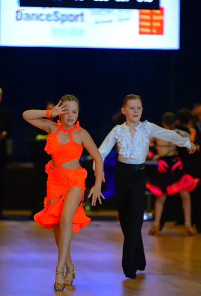 Dancesport competitor: Female dancer in foreground: bright orange latin dance dress with cutouts and a 