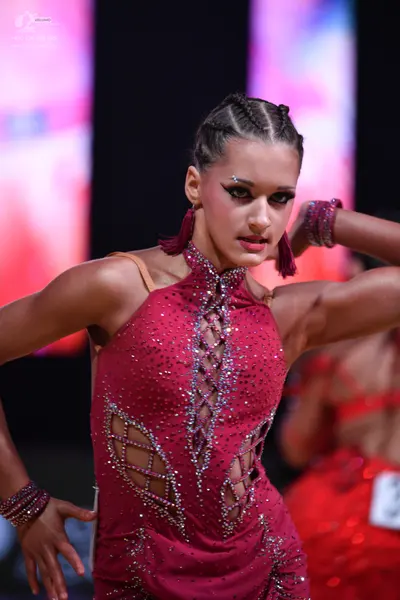 Dancesport competitor: Female dancer (foreground): burgundy latin dress with sequins, mesh cut-outs, an