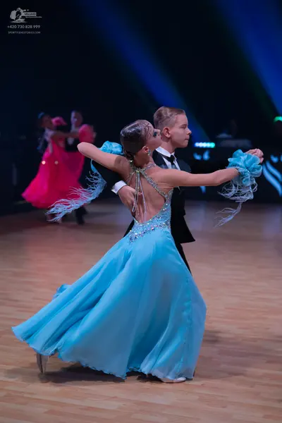 Dancesport competitor: Female dancer in foreground: light blue ballroom gown with a flowing skirt, a se