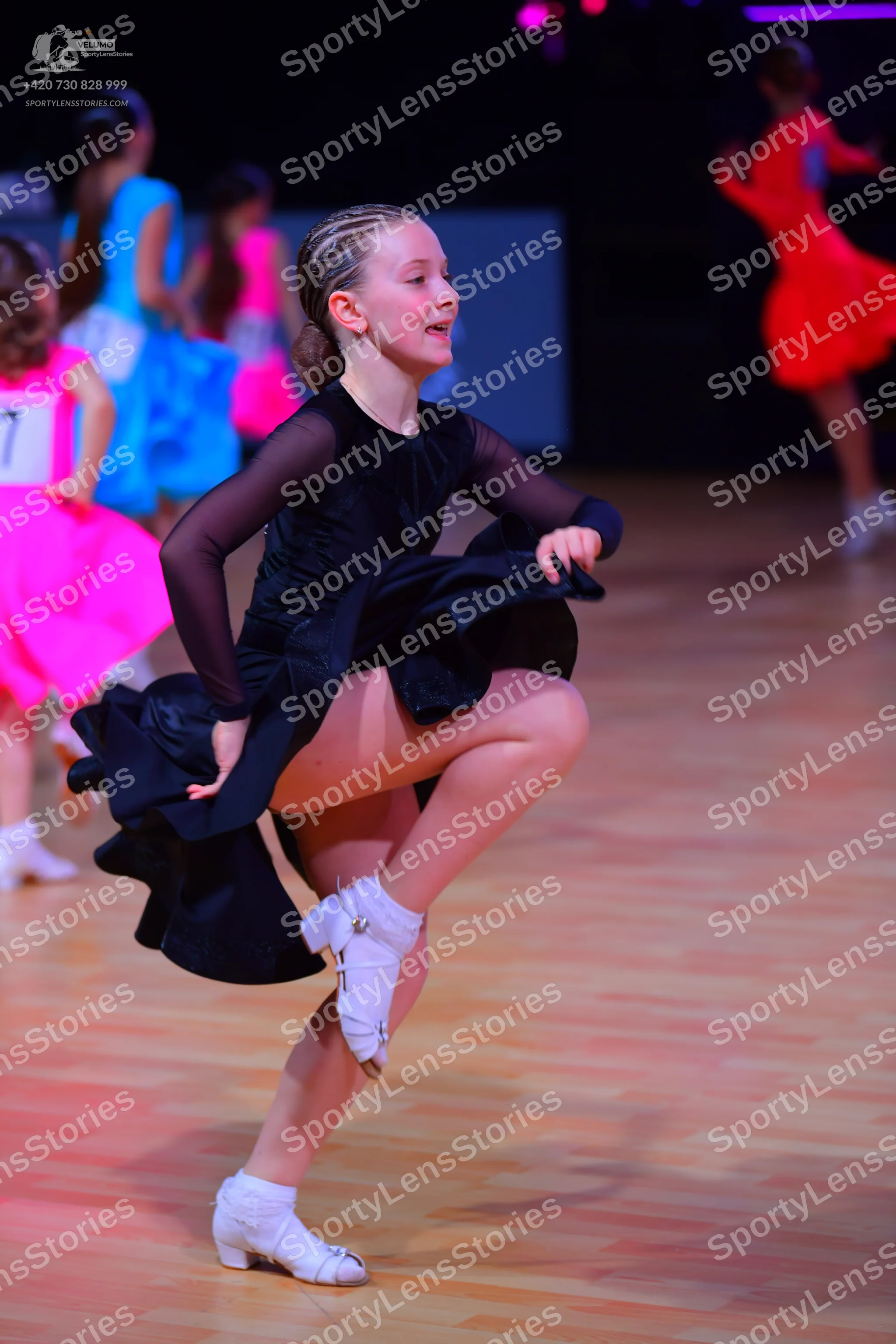 Dancesport competitor: Female dancer in foreground: black long-sleeved dress with sheer sleeves and a f