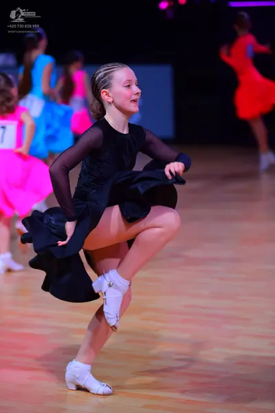 Dancesport competitor: Female dancer in foreground: black long-sleeved dress with sheer sleeves and a f