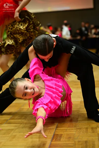 Dancesport competitor: Foreground female dancer: bright pink Latin dance dress with multiple ruffles on