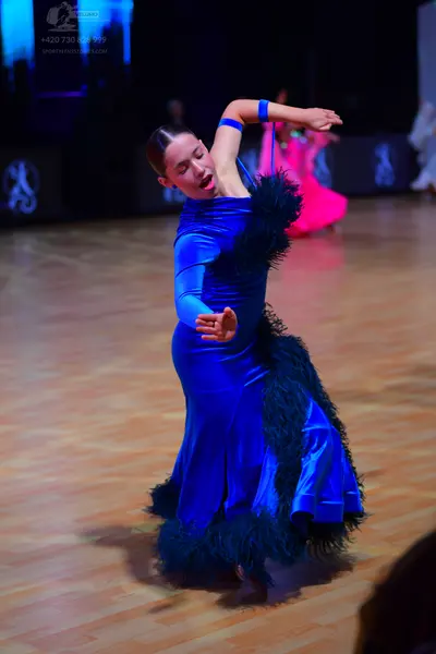 Dancesport competitor: Female dancer: royal blue satin-like long-sleeved gown with large black feather 