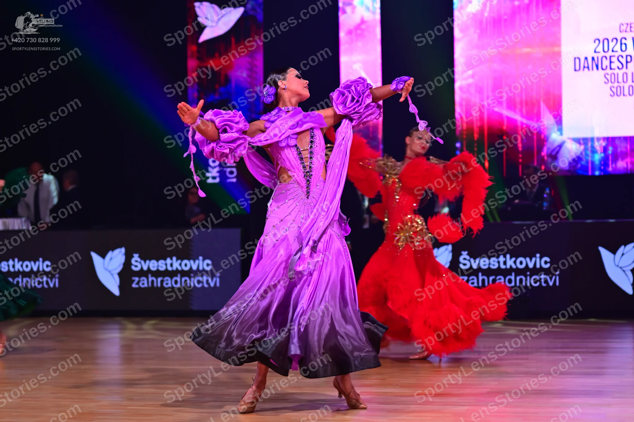 Dancesport competitor: Female dancer 1: lavender ballroom gown with a dark ombré skirt, large ruffled s
