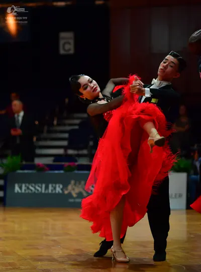 Dancesport competitor: Female dancer: red and black latin dress with a large, ruffled red skirt and tan