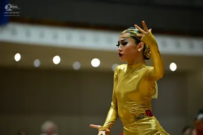Dancesport competitor: Female dancer: gold metallic long-sleeved Latin dress with a high neckline and a