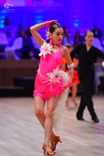 Dancesport competitor: Female dancer: bright pink Latin dress with long fringe and white feather-like e