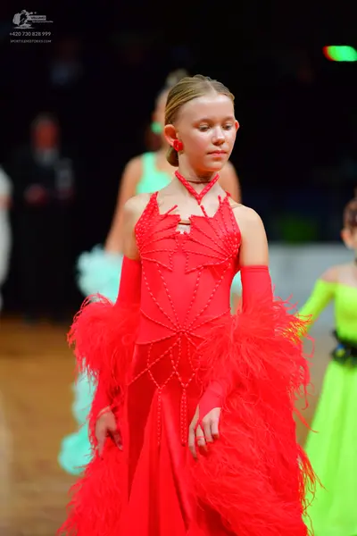 Dancesport competitor: Female dancer in foreground: red Latin dress with red beadwork and large red fea