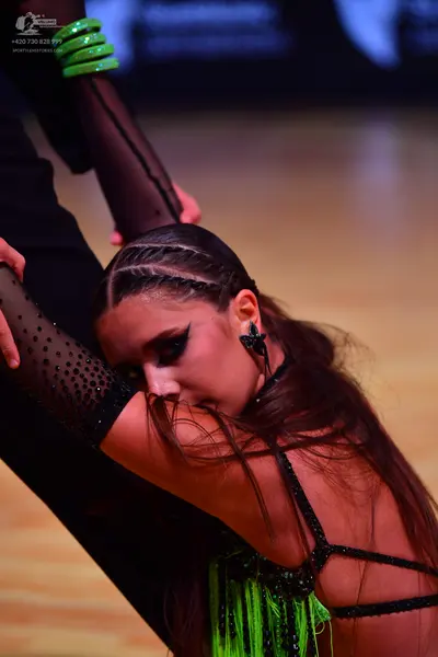 Dancesport competitor: Female dancer: black and lime green latin dress with sheer black sleeves adorned