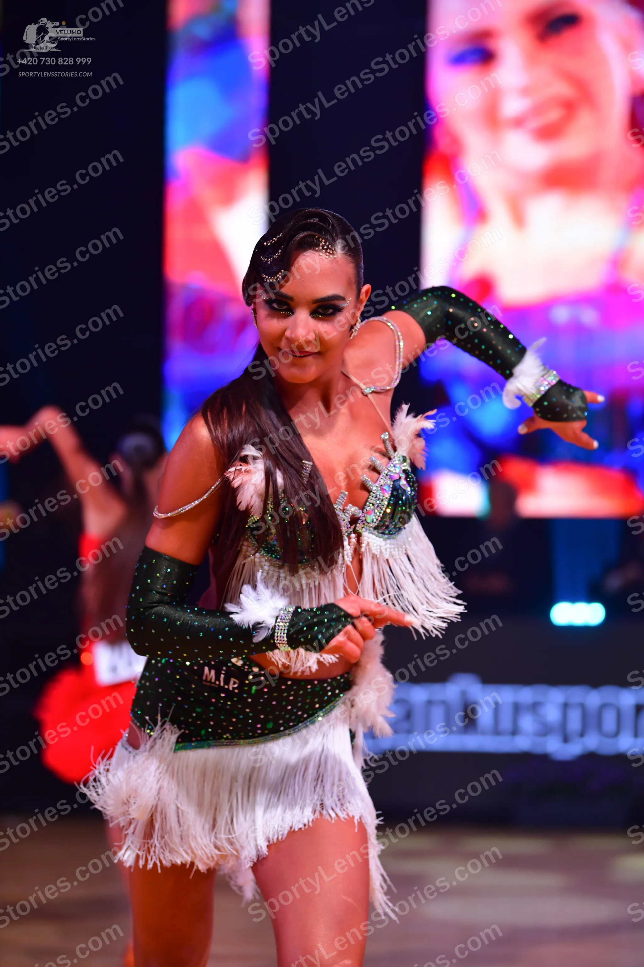 Dancesport competitor: Female dancer in foreground: emerald green latin dress with heavy sequin embelli