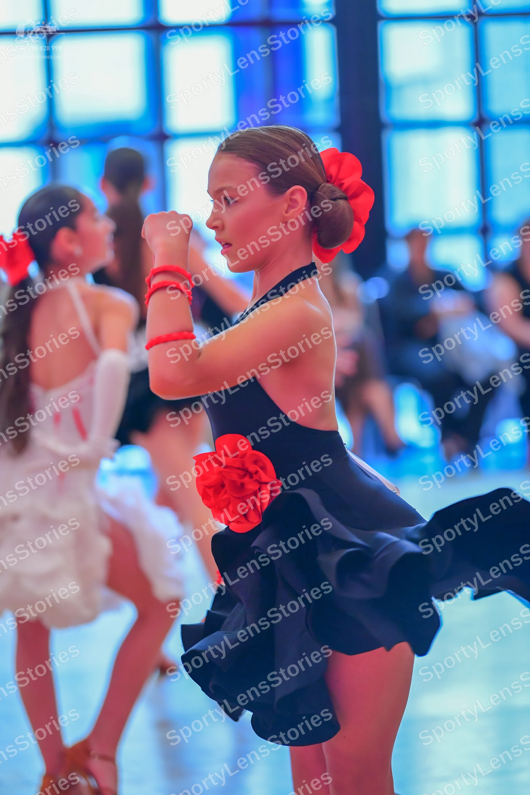 Dancesport competitor: Female dancer in foreground: black Latin dance dress with a ruffled skirt, featu