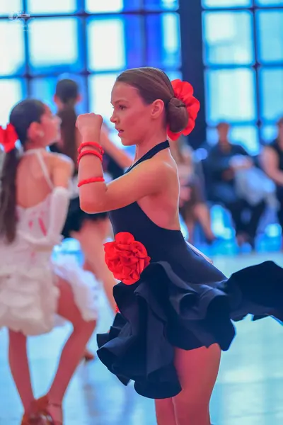 Dancesport competitor: Female dancer in foreground: black Latin dance dress with a ruffled skirt, featu
