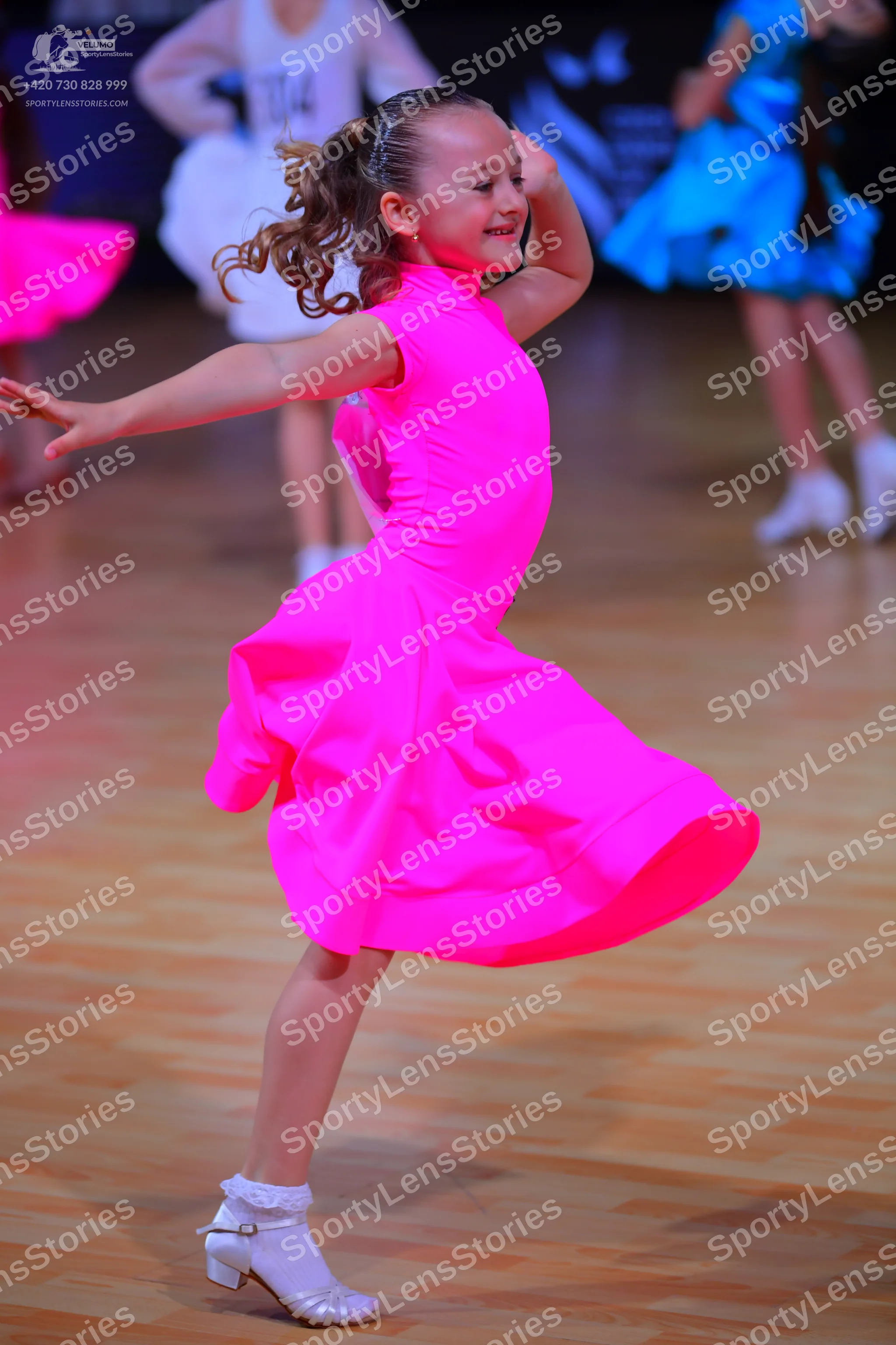 Dancesport competitor: Female dancer in foreground: bright pink sleeveless dress with a voluminous flar