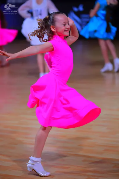 Dancesport competitor: Female dancer in foreground: bright pink sleeveless dress with a voluminous flar
