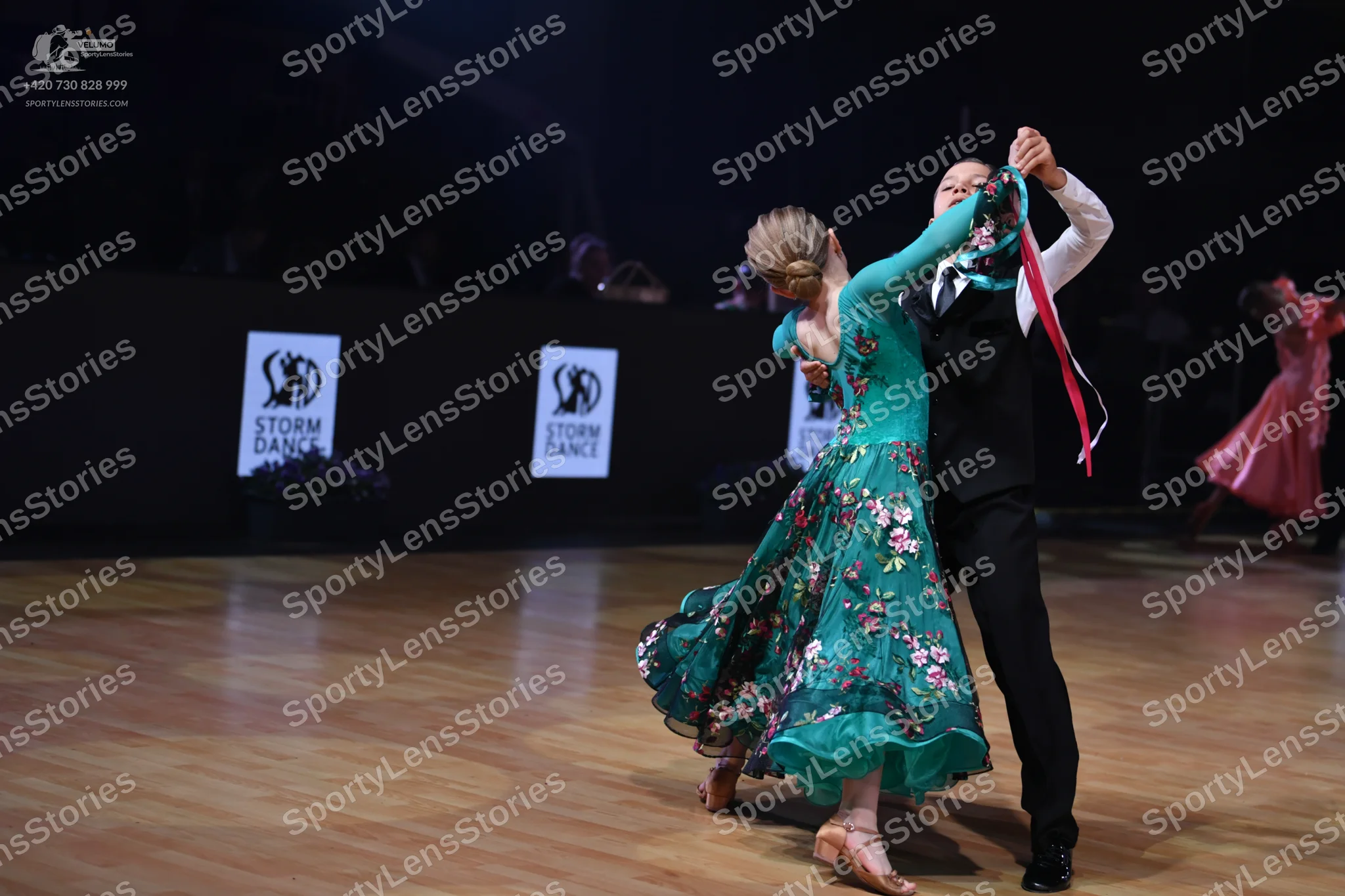 Dancesport competitor: Female dancer: emerald green flowing ballgown with a pink floral pattern and she