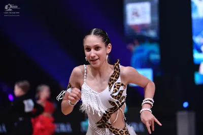 Dancesport competitor: Female dancer (foreground): white Latin dress with leopard print accents, featur