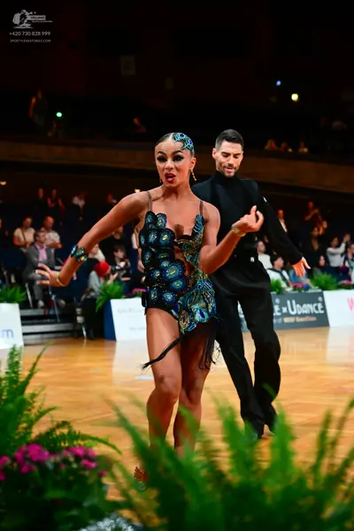 Dancesport competitor: Female dancer: peacock-patterned (teal, blue, and gold) Latin dance bodysuit wit