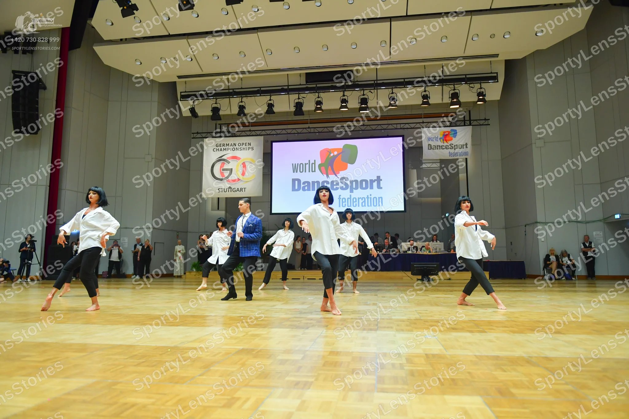 Dancesport competitor: All female dancers are wearing white, loose-fitting long-sleeved blouses and bla
