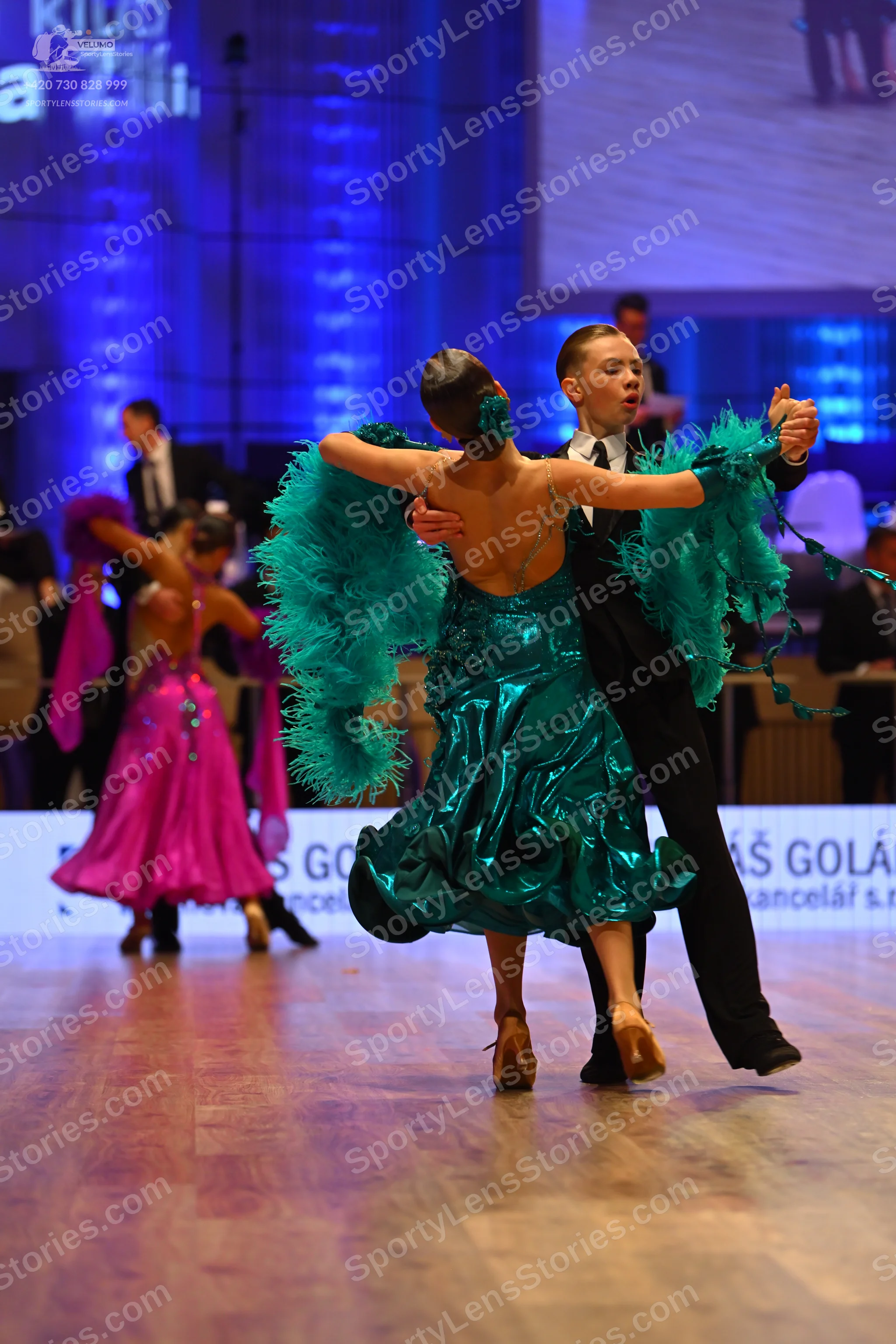 Dancesport competitor: Female dancer in foreground: teal satin latin dress with ruffles and backless de