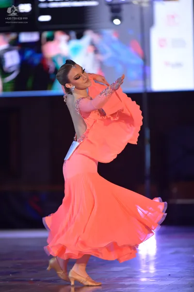Dancesport competitor: Female dancer: coral-colored Latin dress with a long, flowing, ruffled skirt, fe