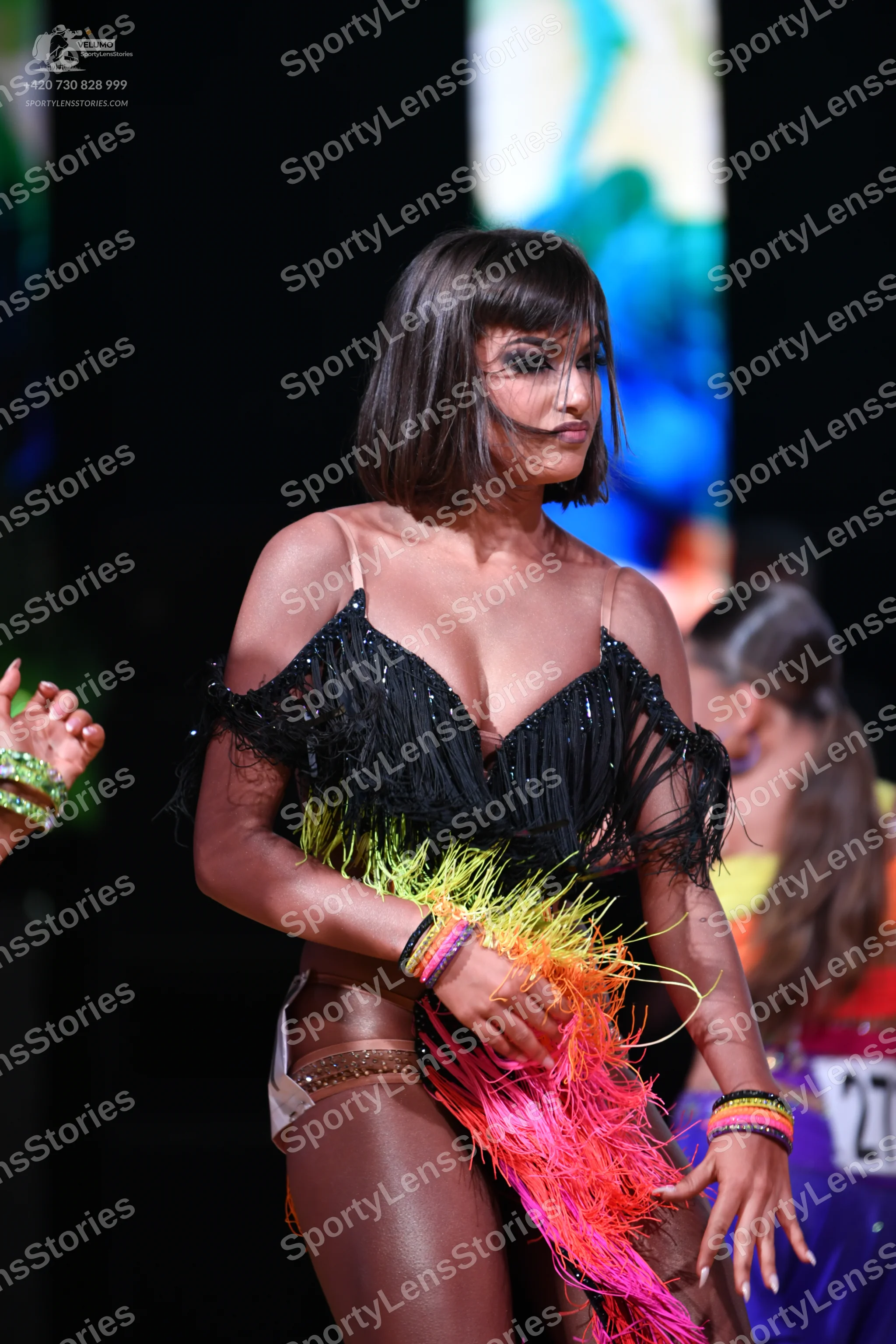 Dancesport competitor: Female dancer in foreground: black latin costume with long, multi-colored fringe