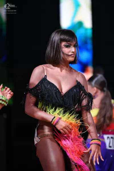 Dancesport competitor: Female dancer in foreground: black latin costume with long, multi-colored fringe